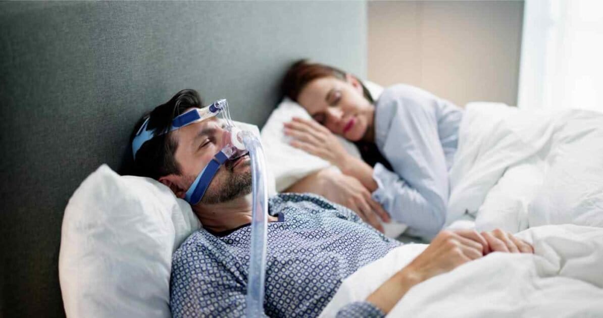 man sleeping with a sleep apnea achine beside his wife